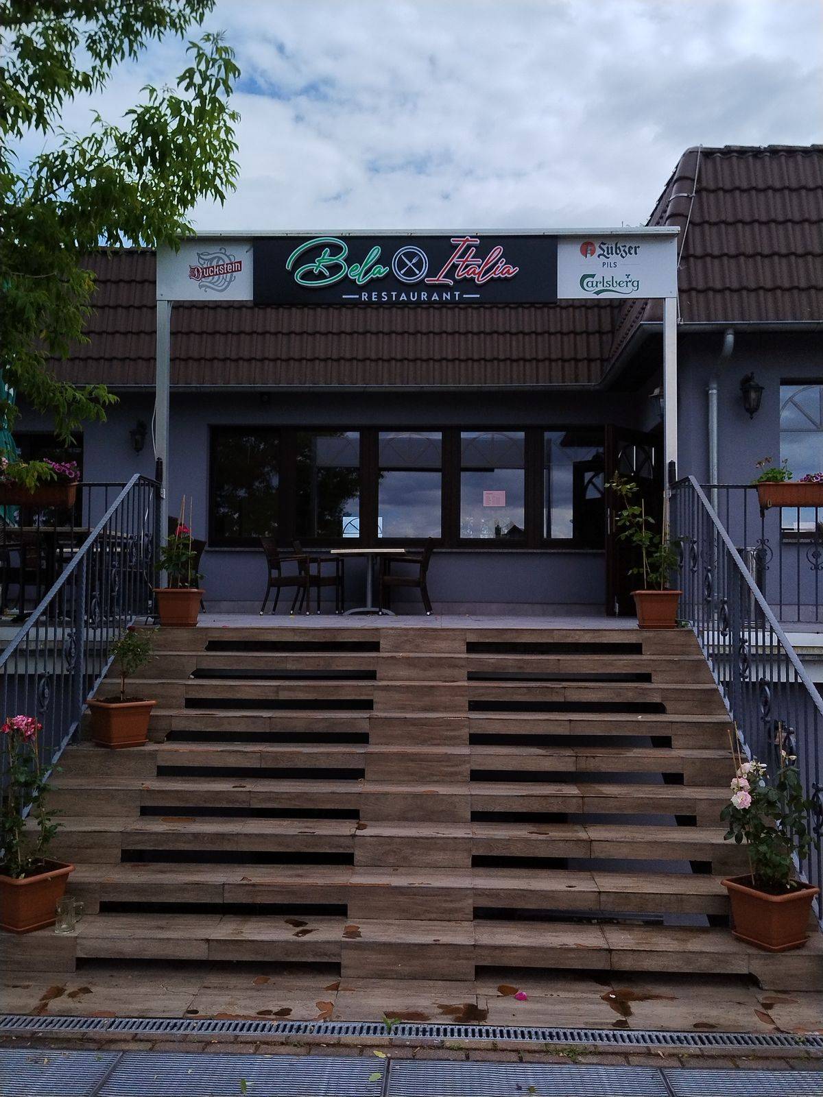 Eingang des Bela Italia mit Treppe und Leuchtschild